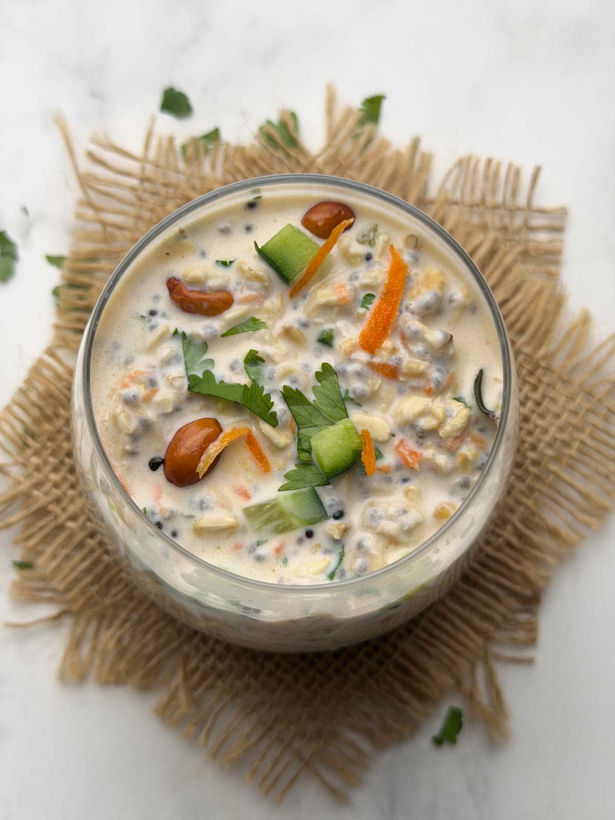 Overnight oats chia tadka in a glass bowl garnished with chopped cucumber, carrot and tempering.