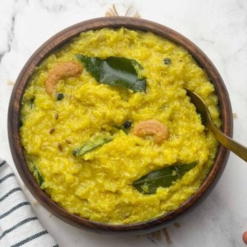 Quinoa pongal served in a brown bowl with golden spoon on it.