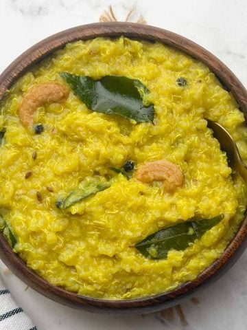 Quinoa pongal served in a brown bowl with golden spoon on it.