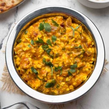 Cottage cheese curry served in a steel serving bowl with boondi raita and paratha on the side.