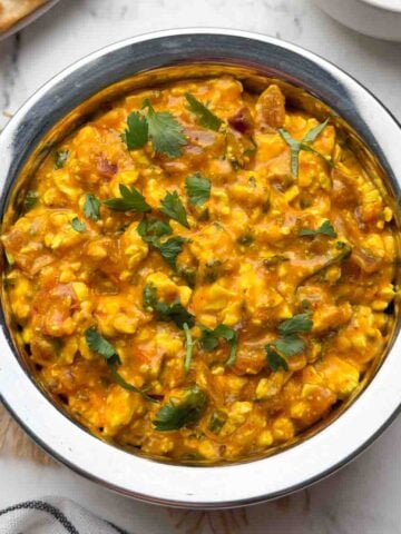 Cottage cheese curry served in a steel serving bowl with boondi raita and paratha on the side.