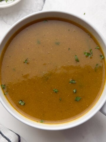 horse gram soup served in a white bowl garnished with cilantro.