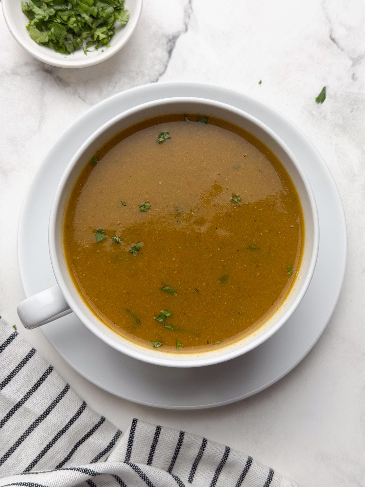 South Indian Horse Gram Soup served in a large white mug, garnished with fresh coriander leaves, with extra coriander on the side.