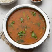 Tomato saaru served in a steel bowl with a bowl of steamed rice and pickle on the side.