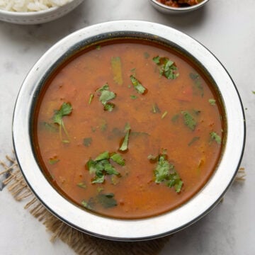 Tomato saaru served in a steel bowl with a bowl of steamed rice and pickle on the side.