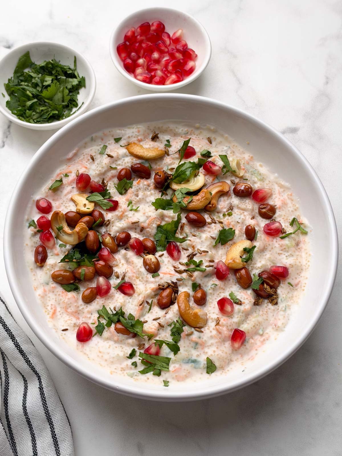 amaranth (rajgira) curd rice served in a white bowl with pomegranate and coriander leaves in small bowl on the side.