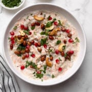 amaranth (rajgira) curd rice served in a white bowl with pomegranate and coriander leaves in small bowl on the side.