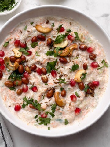 amaranth (rajgira) curd rice served in a white bowl with pomegranate and coriander leaves in small bowl on the side.