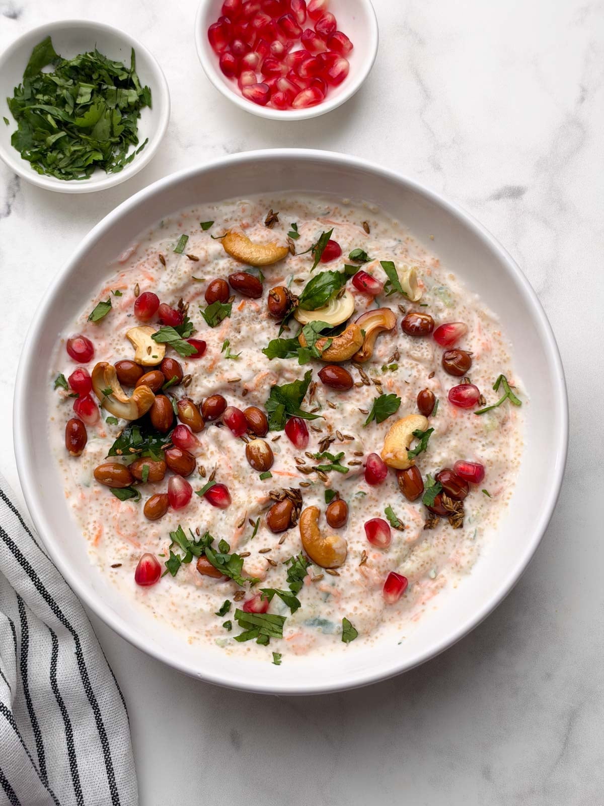 amaranth (rajgira) curd rice served in a white bowl with pomegranate and coriander leaves in small bowl on the side.