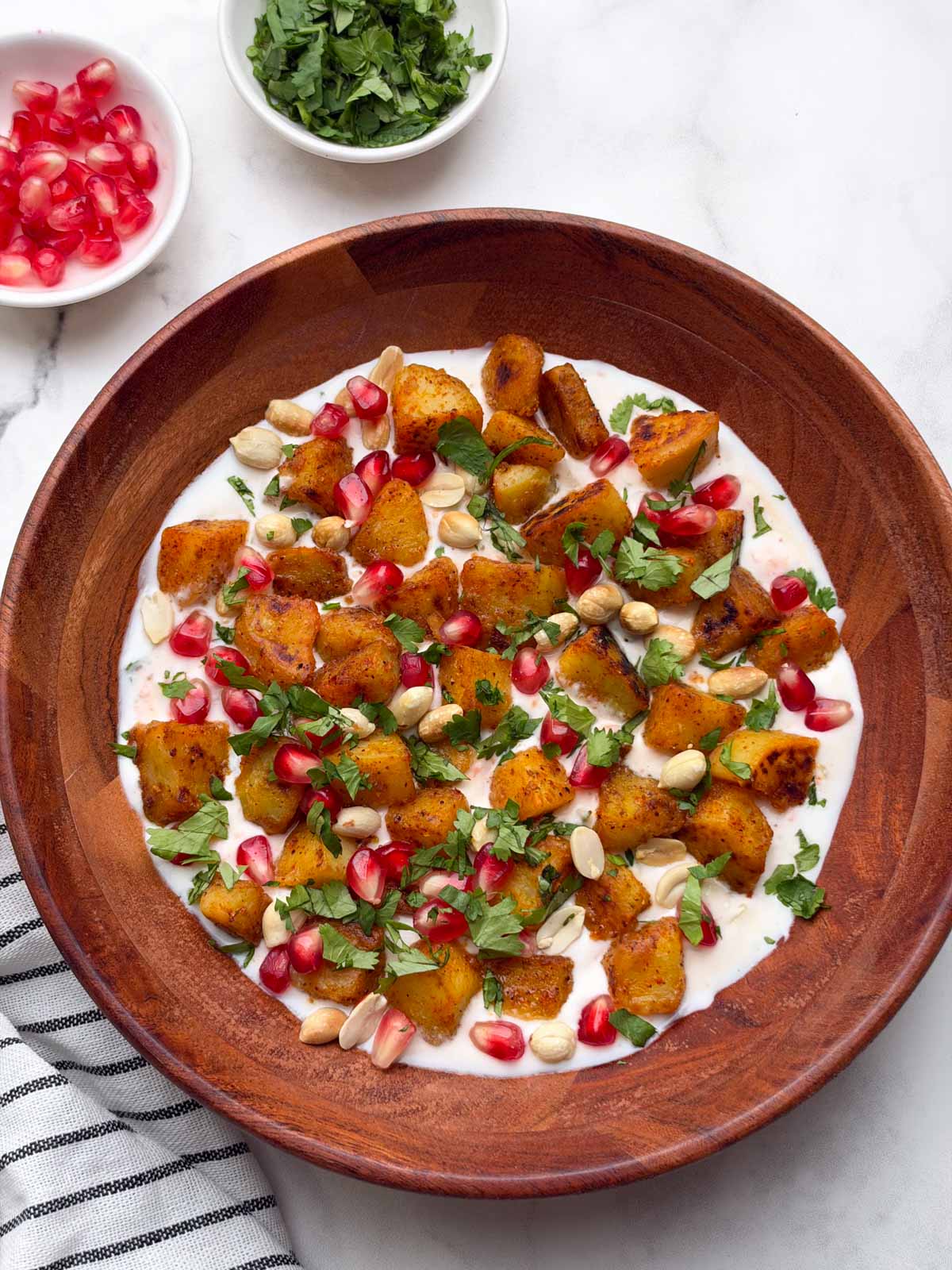 indian style sweet potato chaat served on a wooden bowl with pomegranate seeds and coriander leaves on the side.