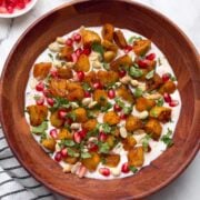 Indian style sweet potato salad served on a wooden bowl with pomegranate seeds and coriander leaves on the side.