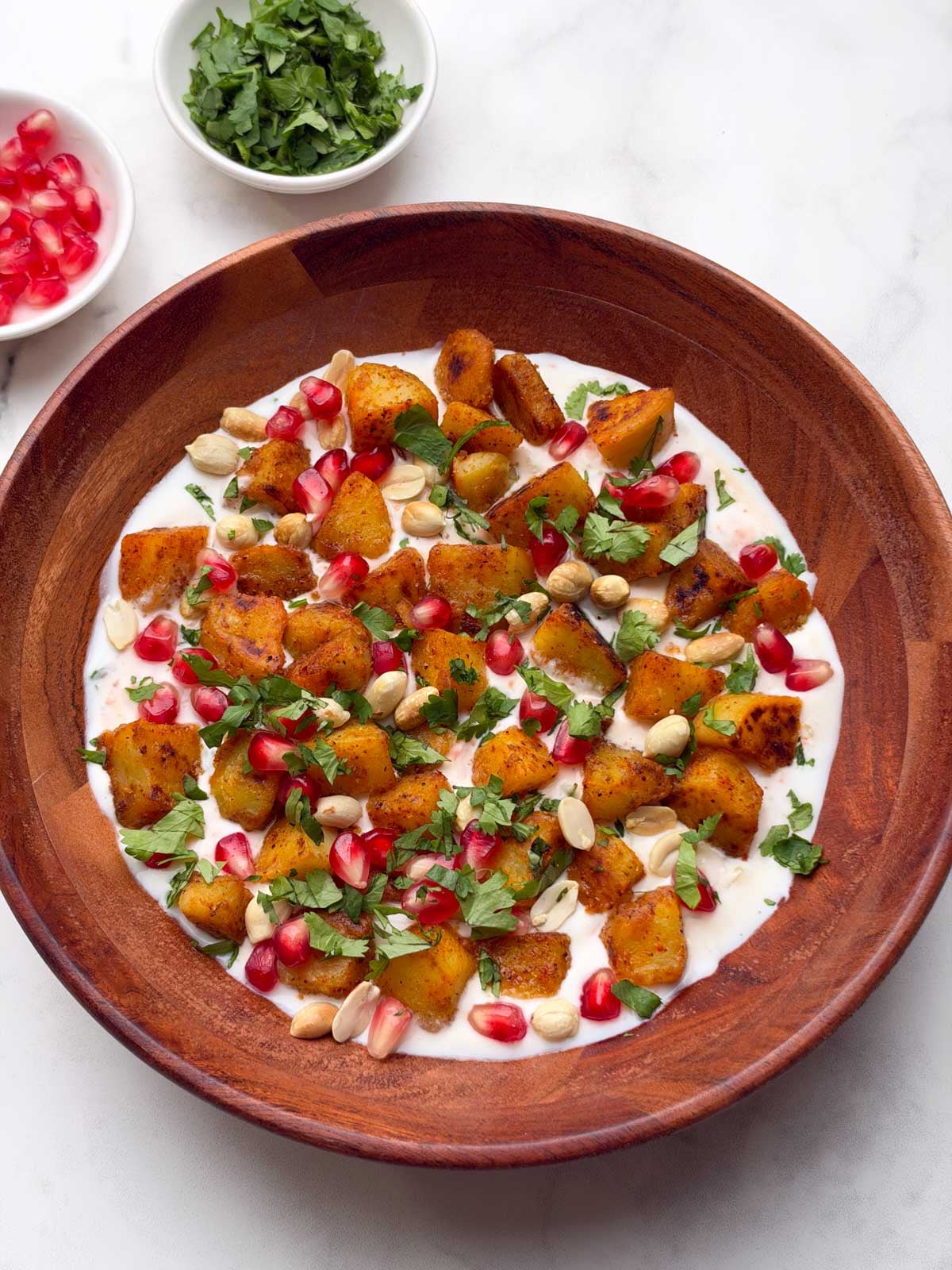 sweet potato salad served on a wooden bowl with pomegranate seeds and coriander leaves on the side.
